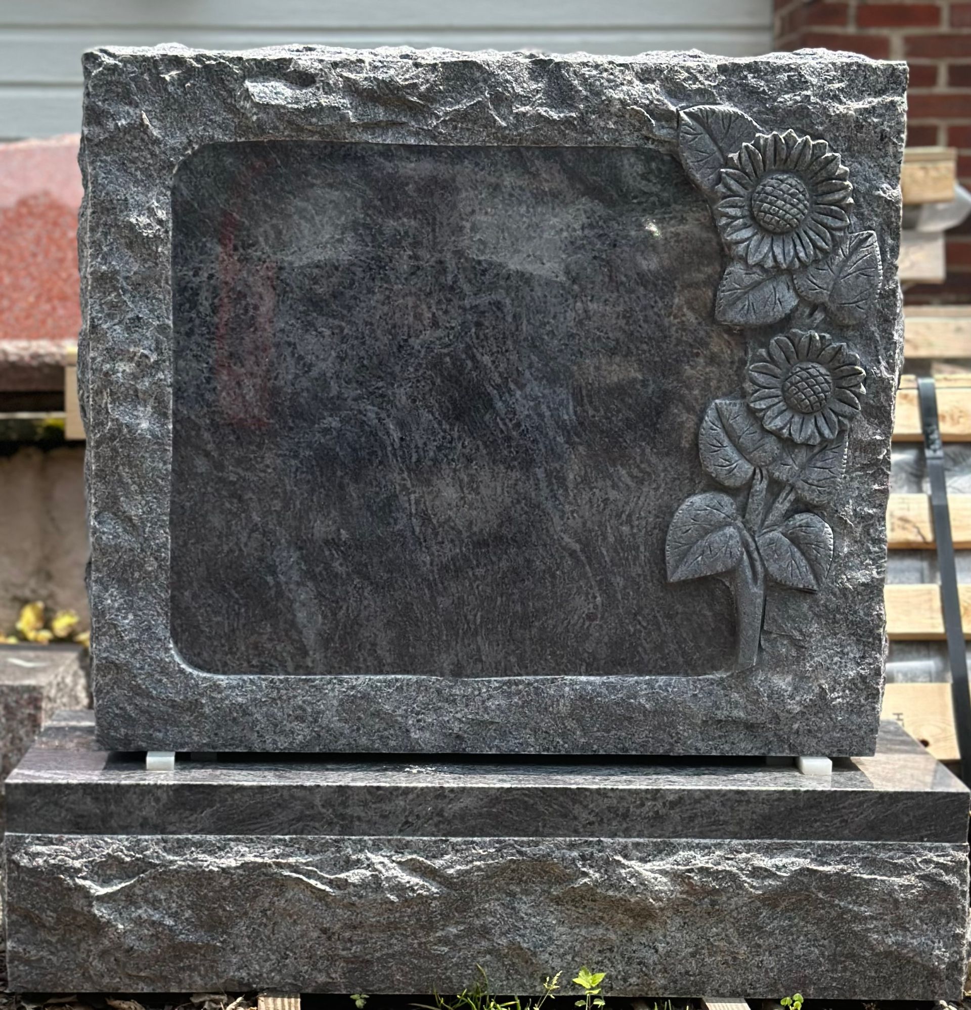 Granite headstone with carved sunflowers, set on a matching base.
