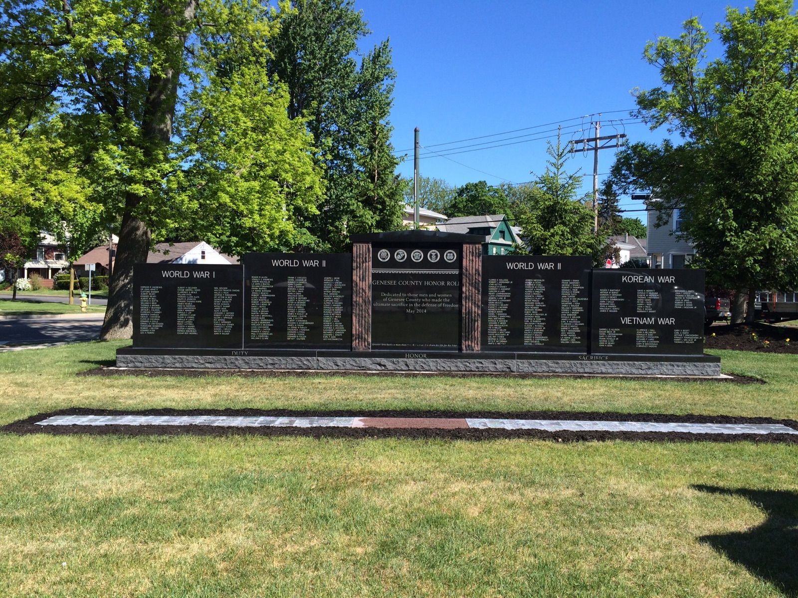 War memorial with black granite panels inscribed with names; set on a grassy lawn.