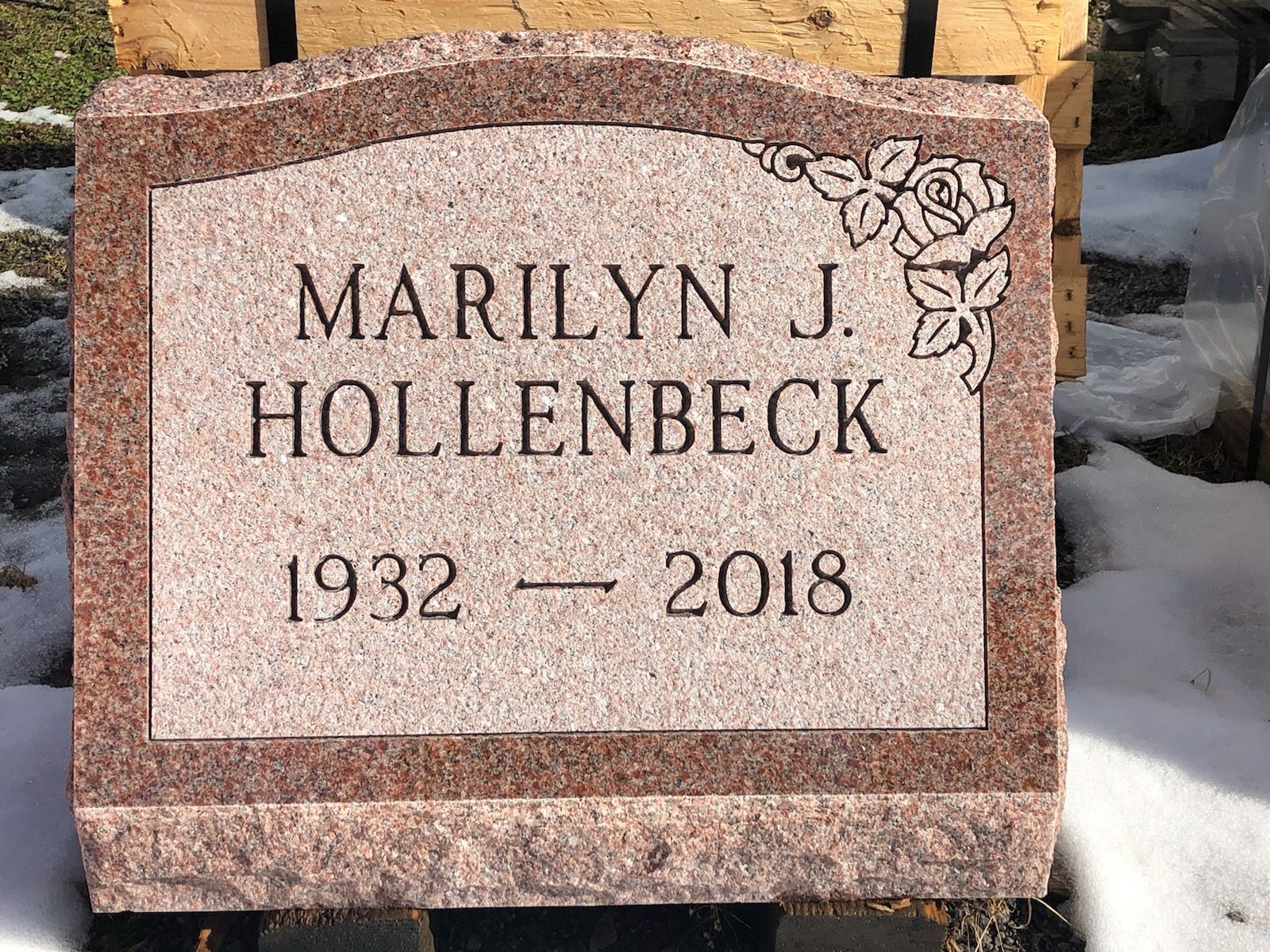 Headstone for Marilyn J. Hollenbeck, with name, birth and death dates, and a rose engraving in red granite.