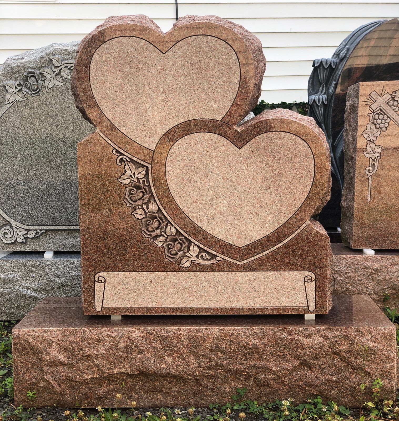 Two heart-shaped headstones with a floral design, on a granite base, outdoors.