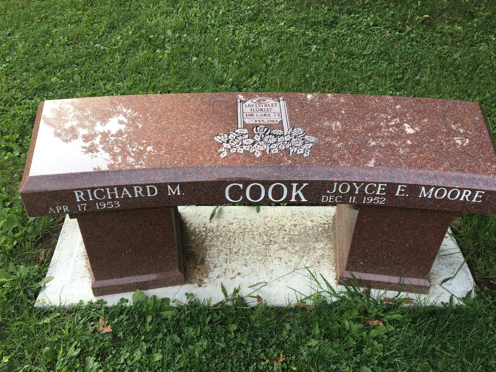 Granite bench with names Richard Cook and Joyce Moore; in a grassy area.