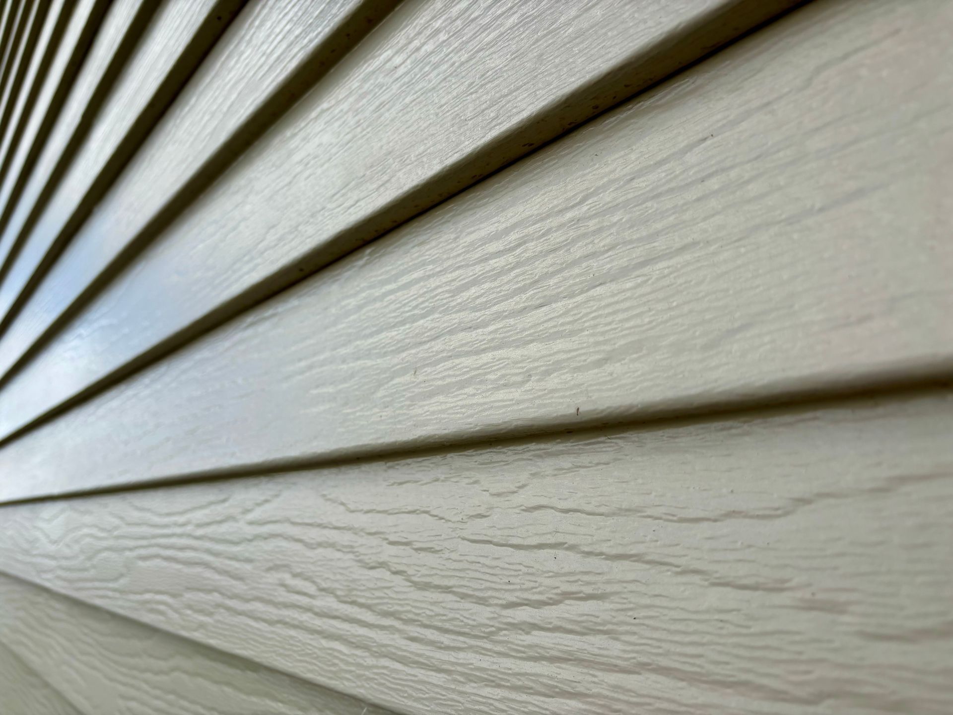 Close-up, angled view of light beige horizontal siding panels with a woodgrain texture.