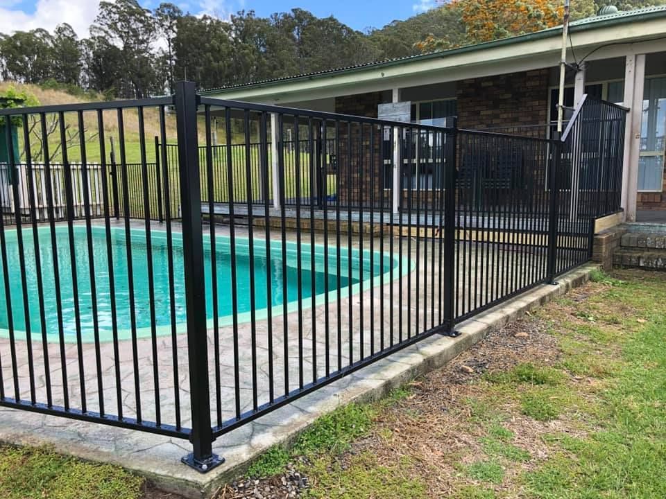 A Black Metal Fence Surrounds a Swimming Pool in Front of A House — Oz-Craft in Port Macquarie, NSW