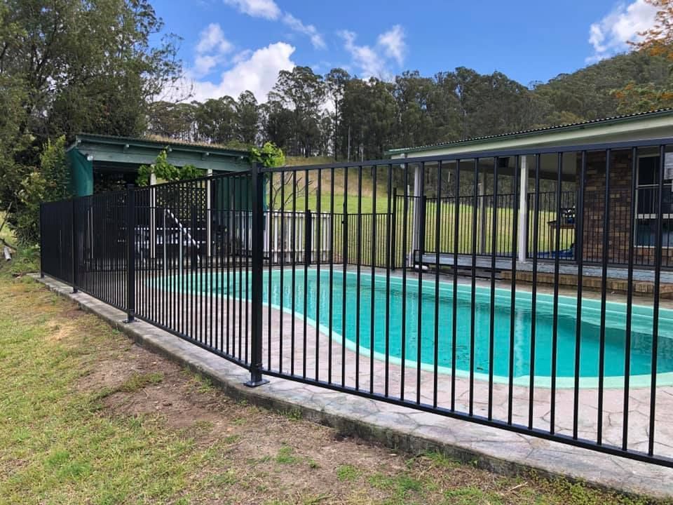 A Black Fence Surrounds a Swimming Pool in Front of A House — Oz-Craft in Forster, NSW