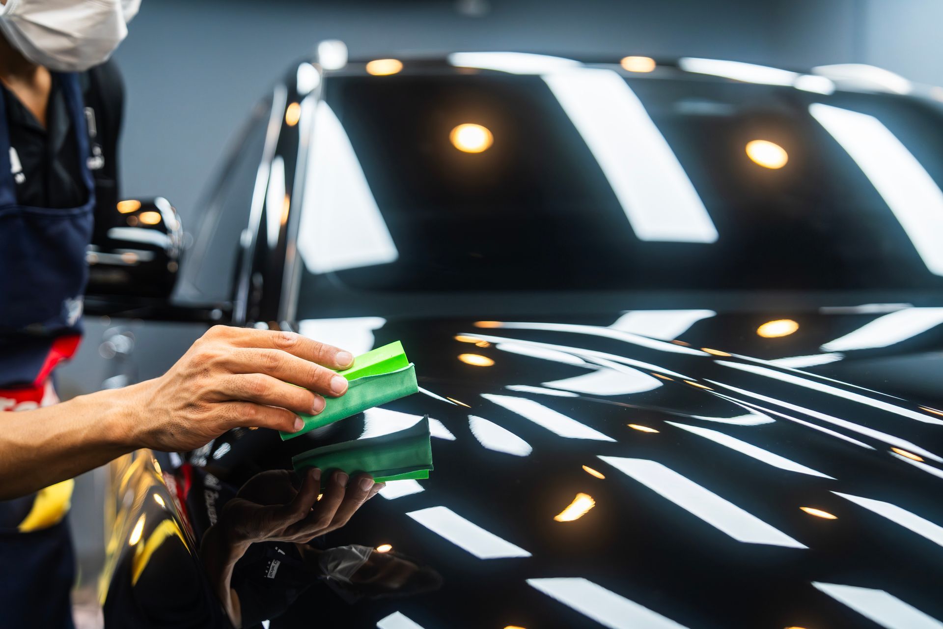 Professional car detailing, hand polishing a black vehicle with a green sponge, shiny finish.