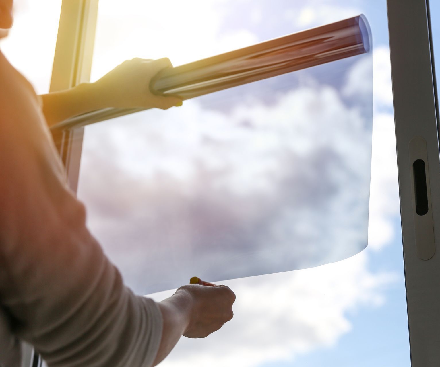 Hands applying residential window tinting film on a sunny window with clear blue skies.