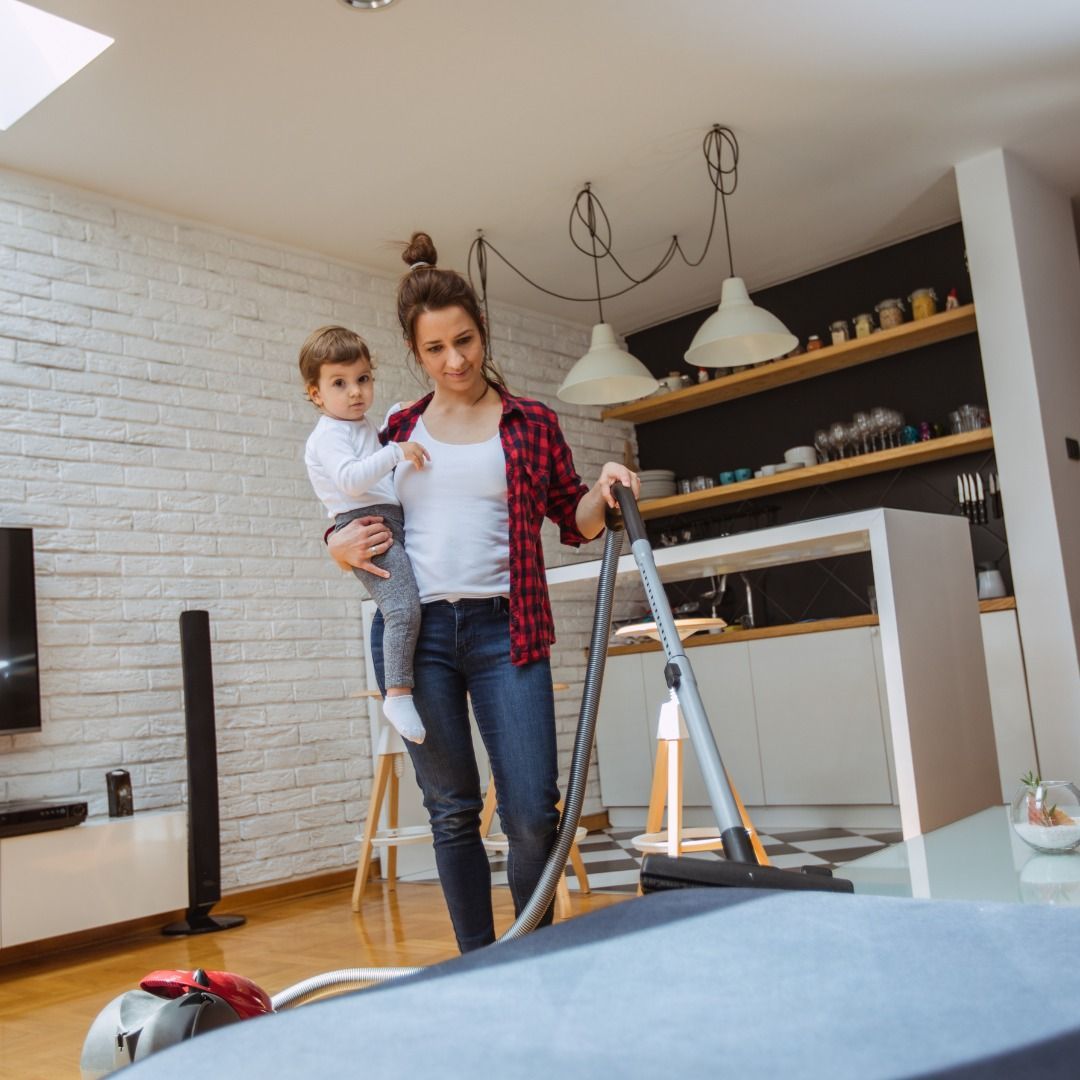 Woman vacuuming while holding a child in a modern living room.