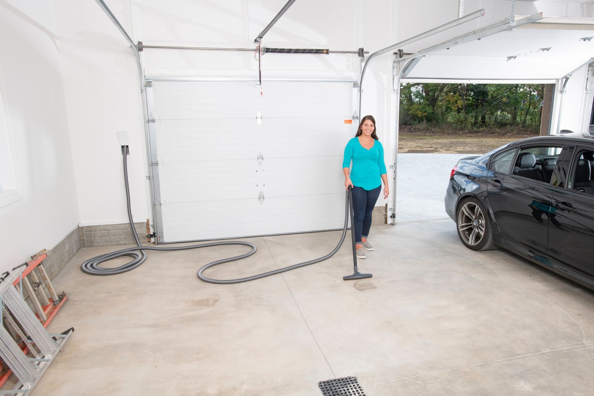 Woman vacuums a garage floor near a car and closed garage door.