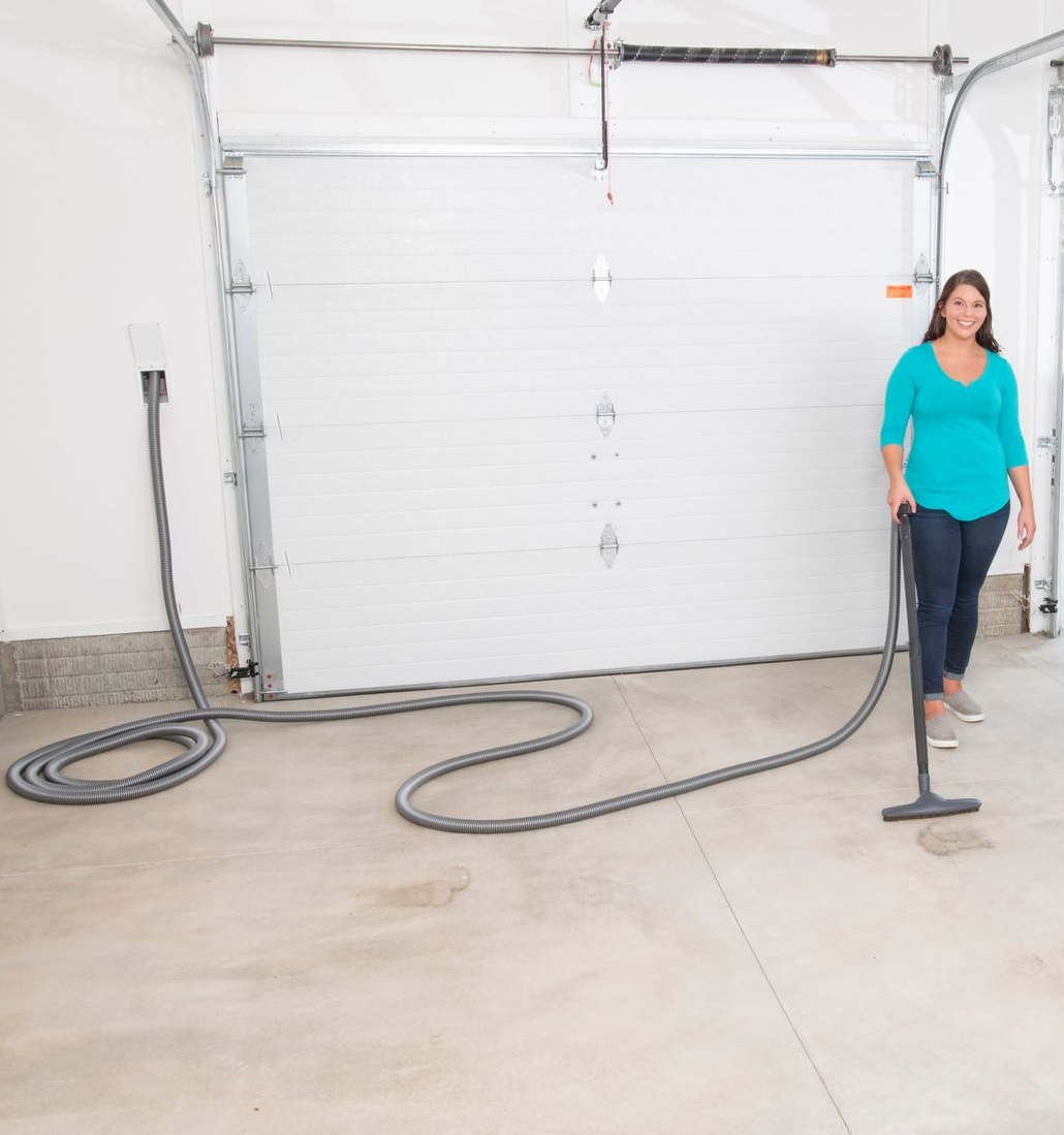 Woman vacuums a garage floor. Vacuum hose is connected to a wall outlet.