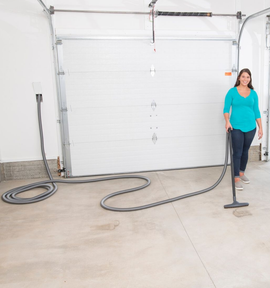 Woman vacuums a garage floor. Vacuum hose is connected to a wall outlet.