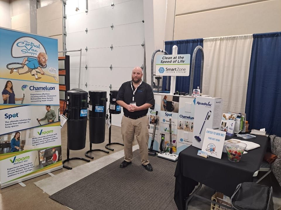 Man in booth at trade show, surrounded by vacuum products and displays.