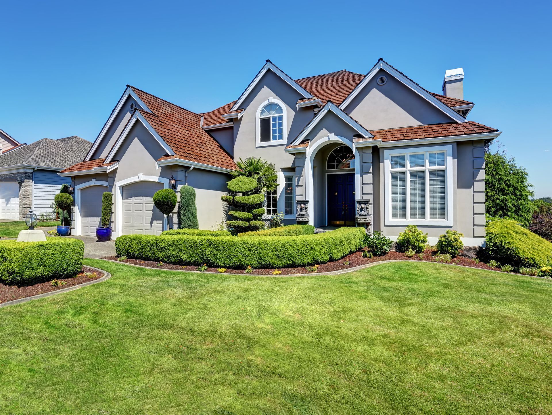 Gray house with brown roof, blue door, white trim, and well-manicured green lawn.