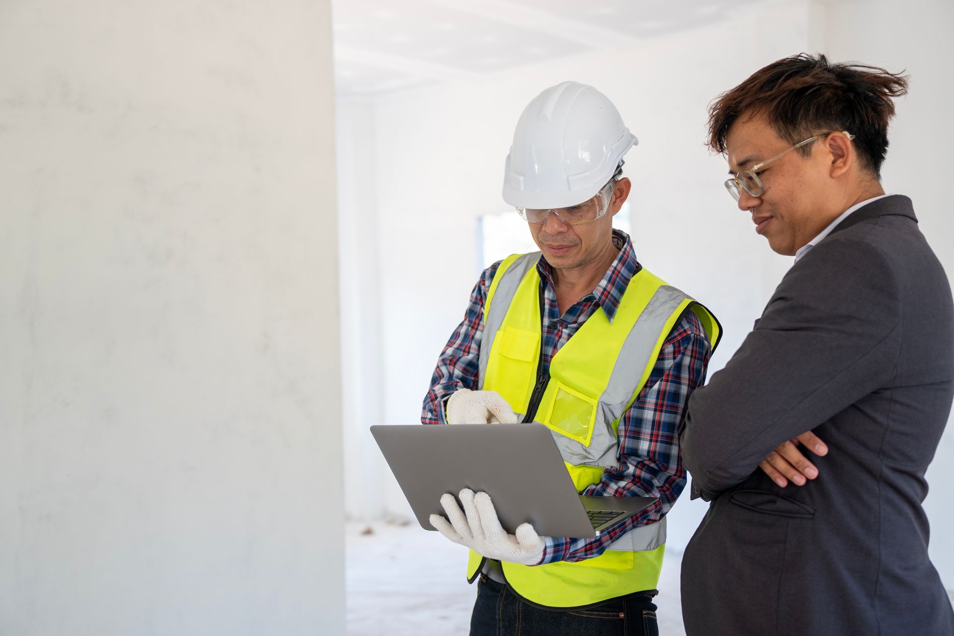 Construction worker and businessman looking at a laptop in a building under construction.