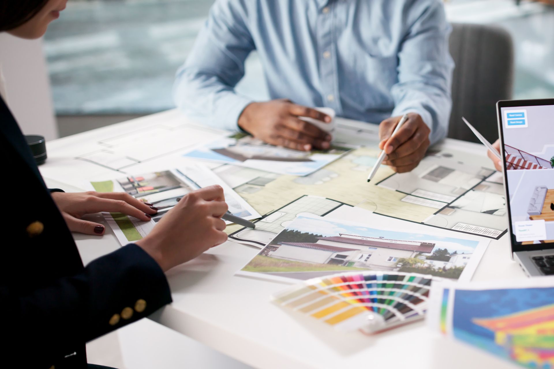 People reviewing architectural plans, color swatches, and images on a laptop.