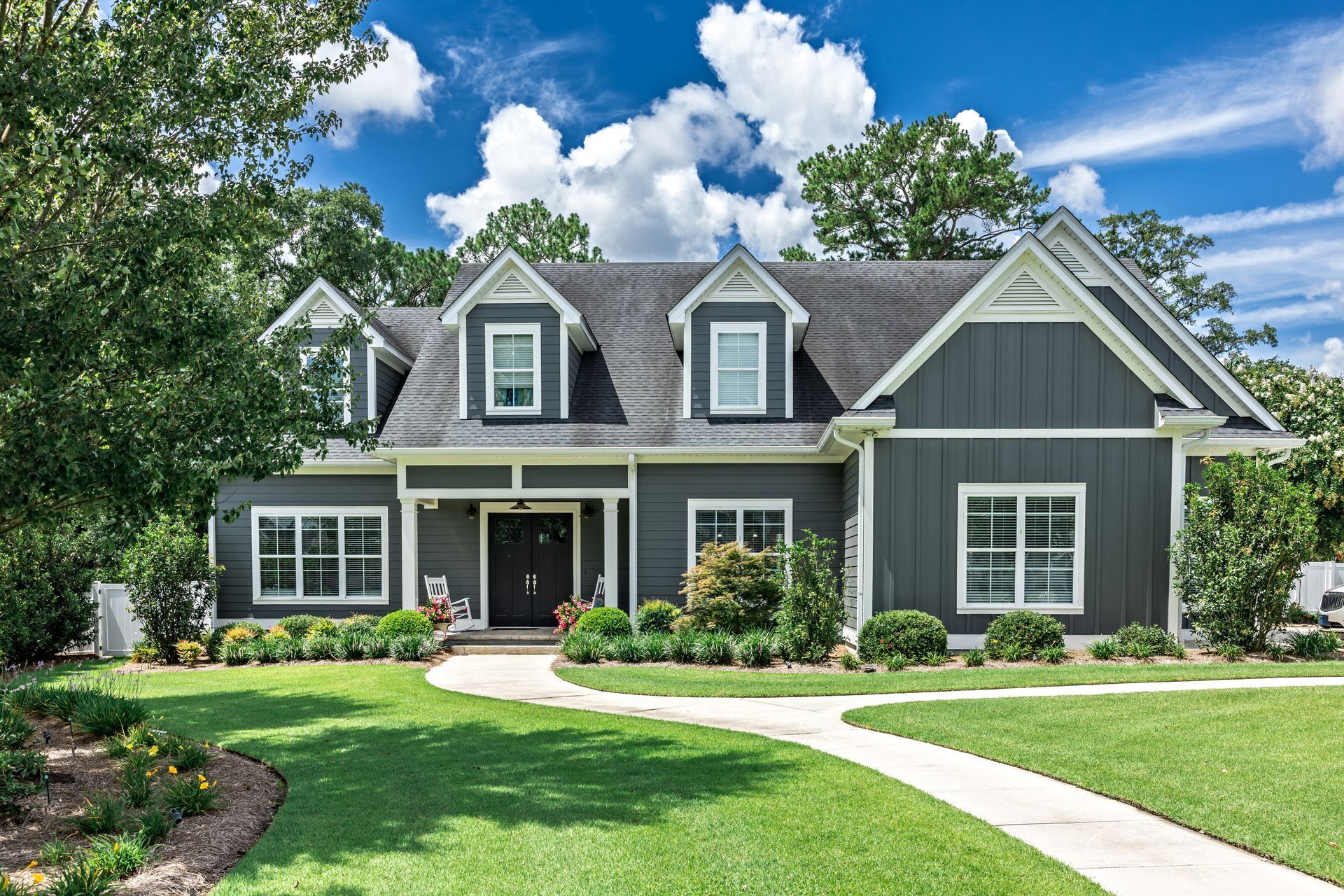 Gray house with white trim, dormers, and a curving walkway through a green lawn.