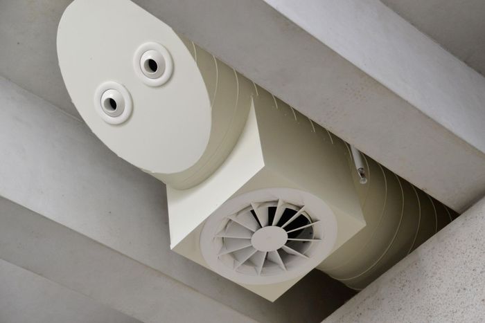 A white duct with a fan attached to it is hanging from the ceiling.