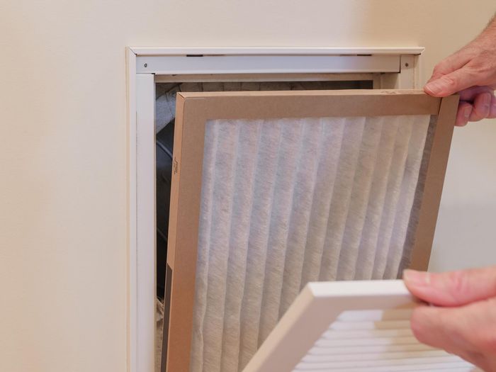 A person is taking a filter out of a wall vent.