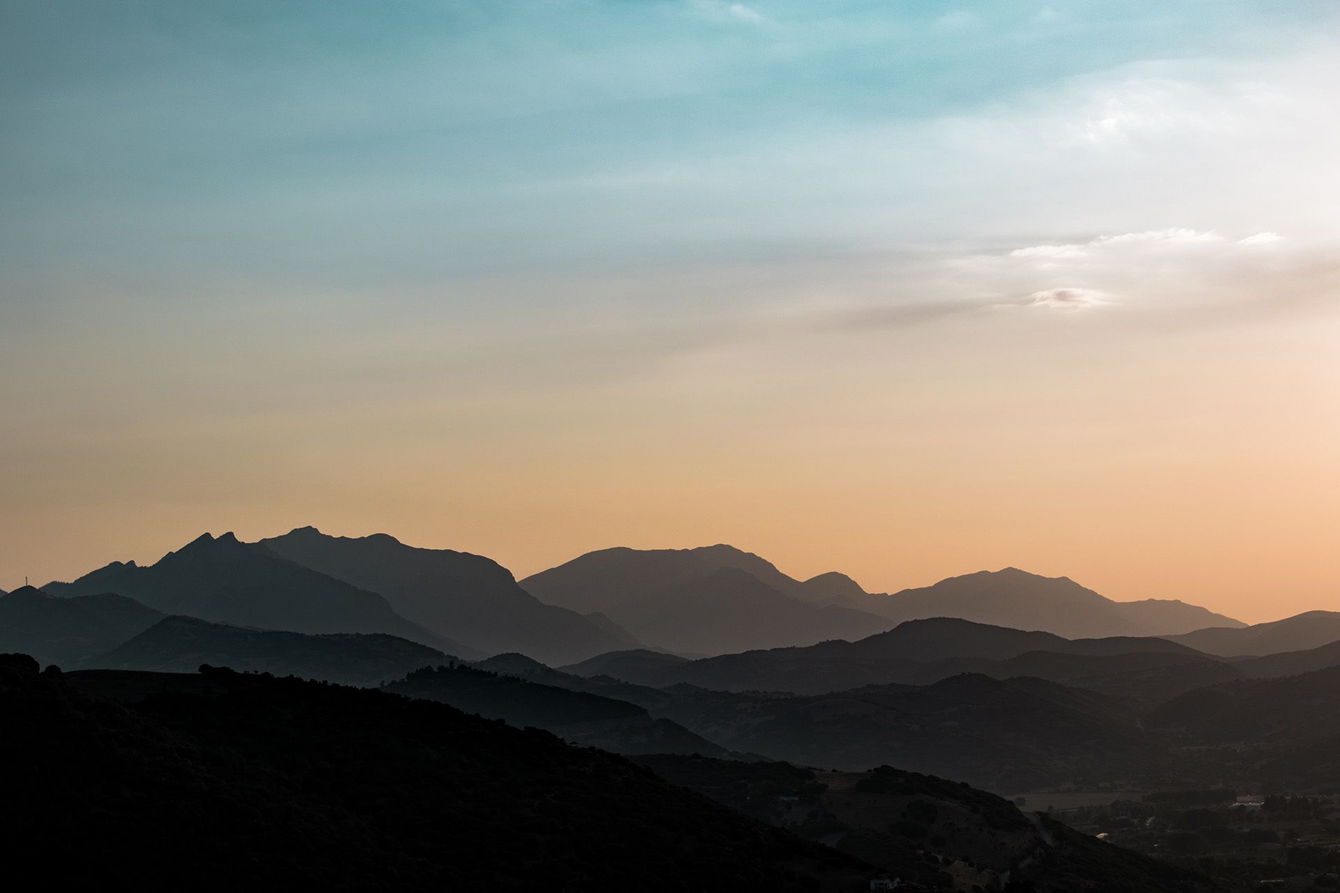 Layers of silhouetted mountain ridges fade into the distance against a soft, gradient sky at sunset.