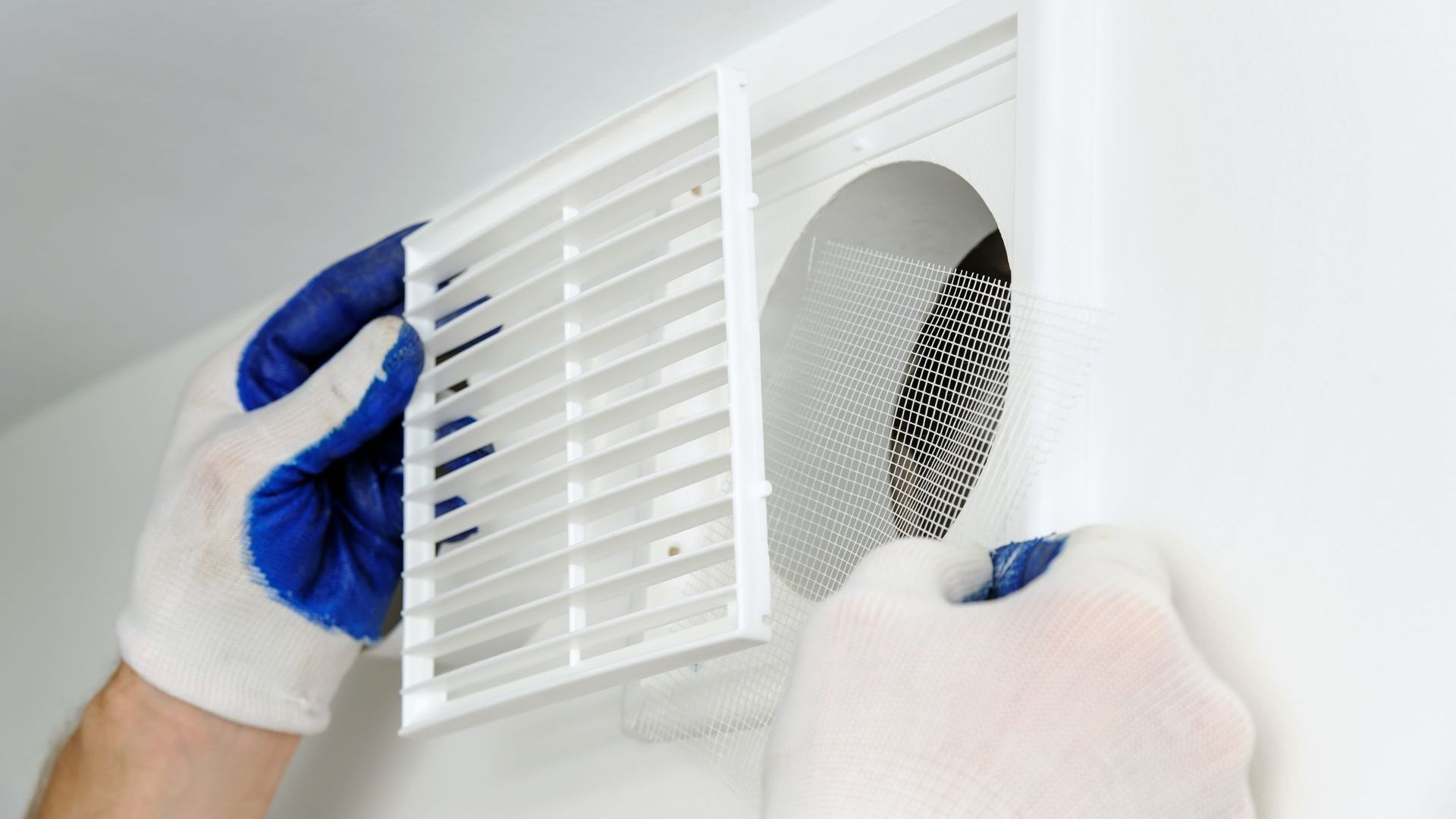 A person wearing blue gloves is fixing a vent on a wall.