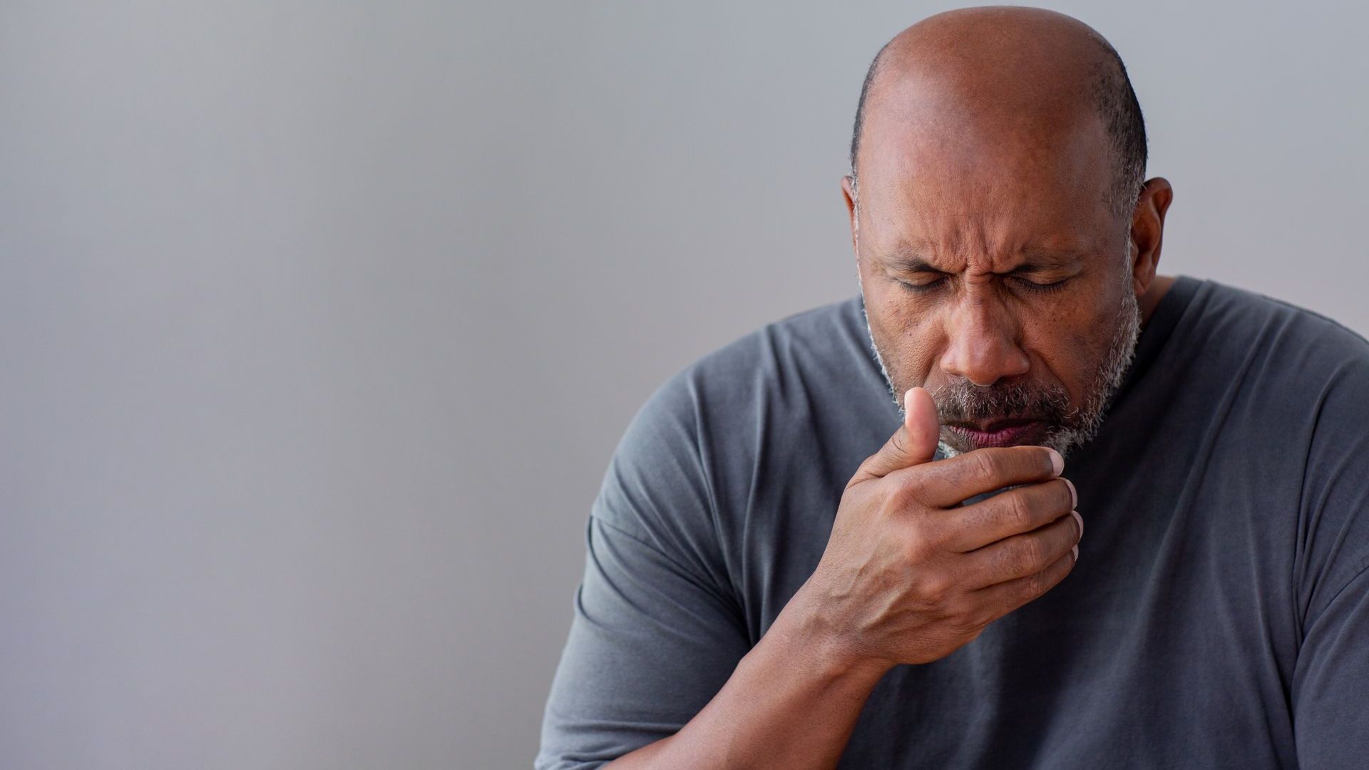 A man with a beard is coughing into his hand.