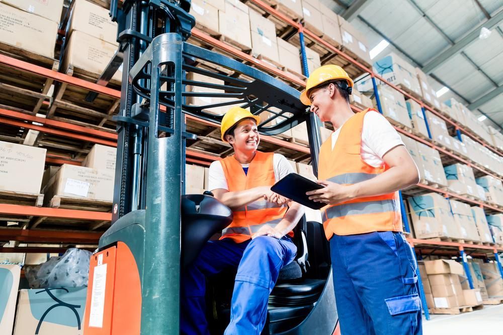 Man is Sitting in a Forklift in a Warehouse Talking to Another Man — Bundaberg Forklift Repairs Childers, QLD