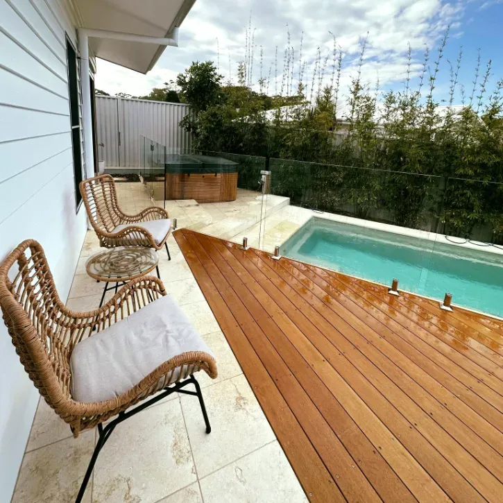 A wooden deck with chairs and a table next to a swimming pool — Mid Coast Glass Fencing In Bonny Hills, NSW