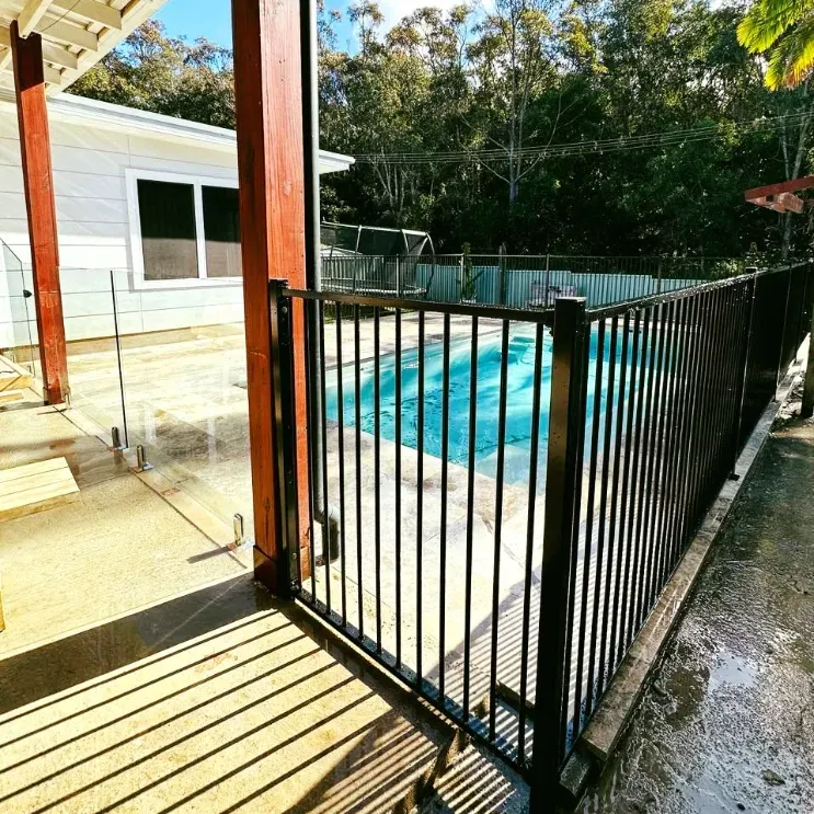 A Black Fence Surrounds A Swimming Pool Next To A HoUSE — Mid Coast Glass Fencing In Laurieton, NSW