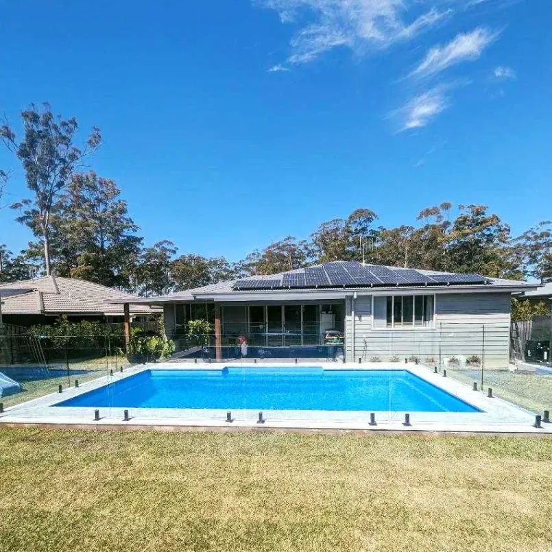 A large swimming pool in front of a house with solar panels on the roof — Mid Coast Glass Fencing In Laurieton, NSW