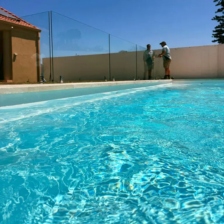 Two people standing on the edge of a swimming pool — Mid Coast Glass Fencing In Laurieton, NSW