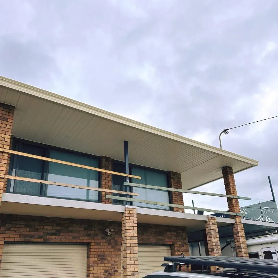 A brick building with a balcony and a car parked in front of it — Mid Coast Glass Fencing In Hallidays Point, NSW