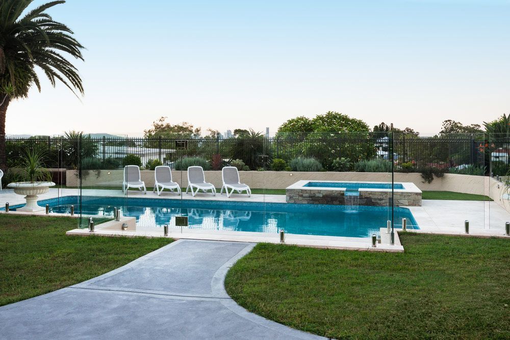 A large swimming pool surrounded by chairs and a palm tree — Mid Coast Glass Fencing In Wauchope, NSW