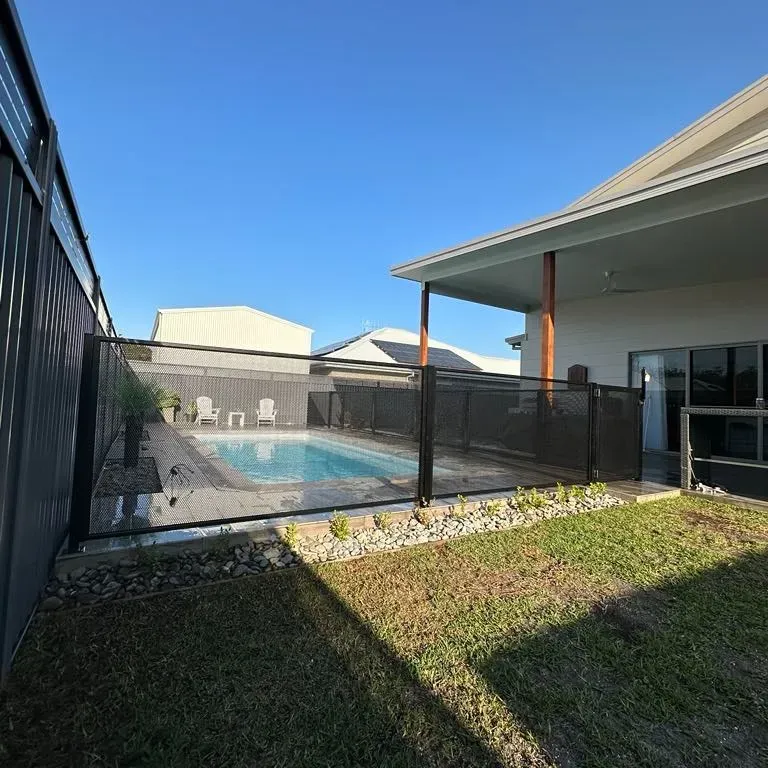 A Fence Surrounds A Swimming Pool In The Backyard Of A HoUSE — Mid Coast Glass Fencing In Laurieton, NSW