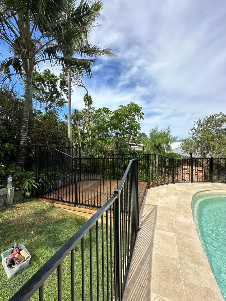 A Black Metal Fence Surrounds A Swimming Pool In A BackyARD — Mid Coast Glass Fencing In South West Rocks, NSW