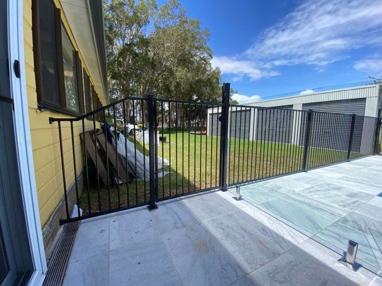 A black fence is surrounding a swimming pool in front of a house — Mid Coast Glass Fencing In Old Bar, NSW