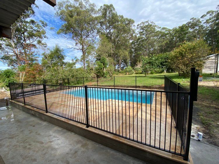 A Fence Surrounds A Swimming Pool In A Backyard — Mid Coast Glass Fencing In Old Bar, NSW