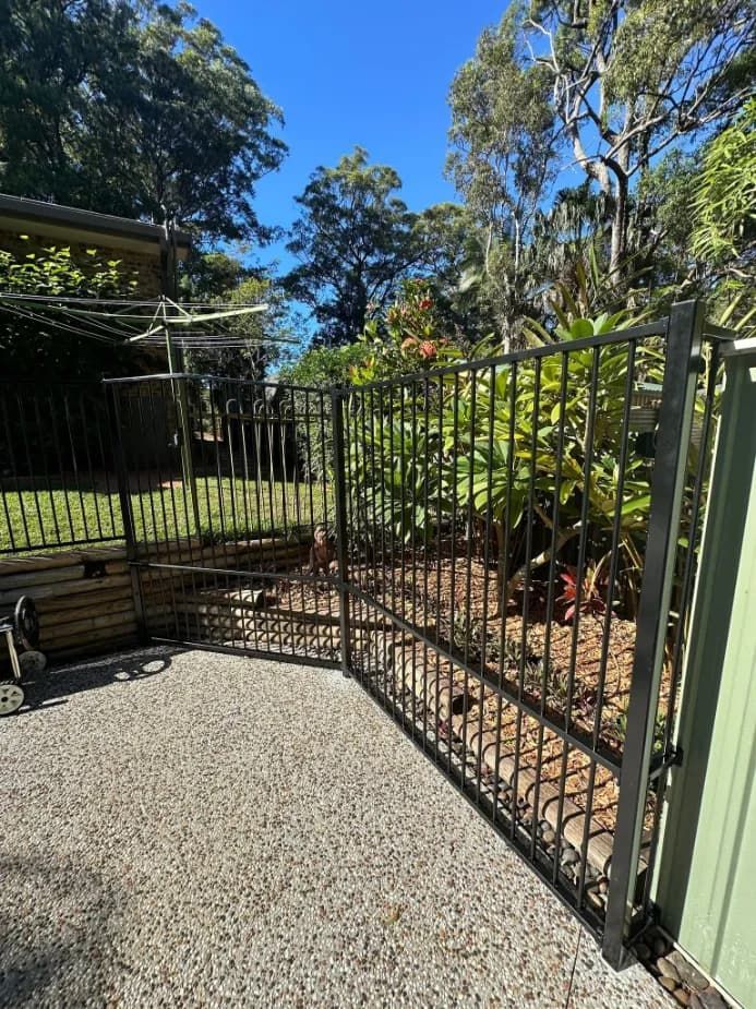 A Metal Gate Is Surrounded By Gravel And Trees In A YARD — Mid Coast Glass Fencing In Wauchope, NSW