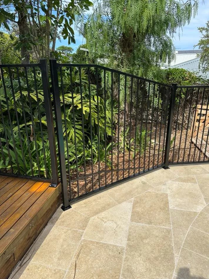A Black Metal Fence Is Surrounding A Wooden DECK — Mid Coast Glass Fencing In Wauchope, NSW
