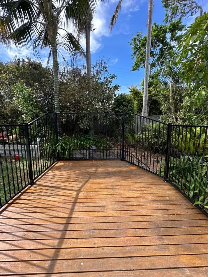 A wooden deck with a metal railing and palm trees in the background — Mid Coast Glass Fencing In Wauchope, NSW