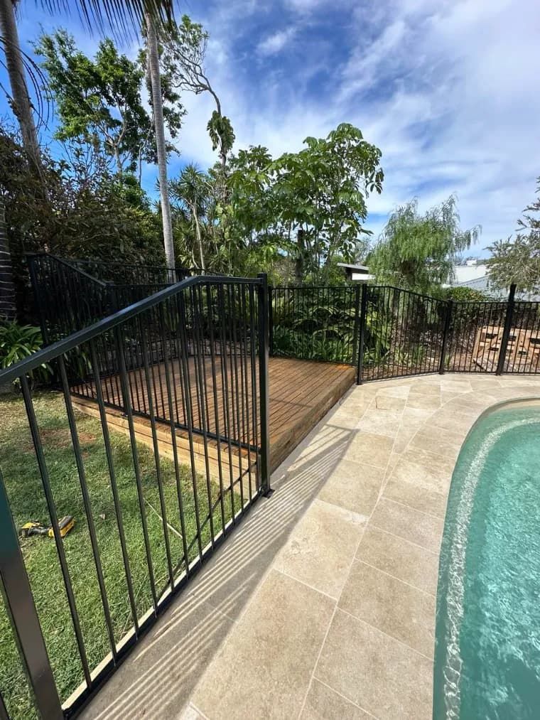 A Fence Surrounds A Swimming Pool With A Wooden DECK — Mid Coast Glass Fencing In Hallidays Point, NSW