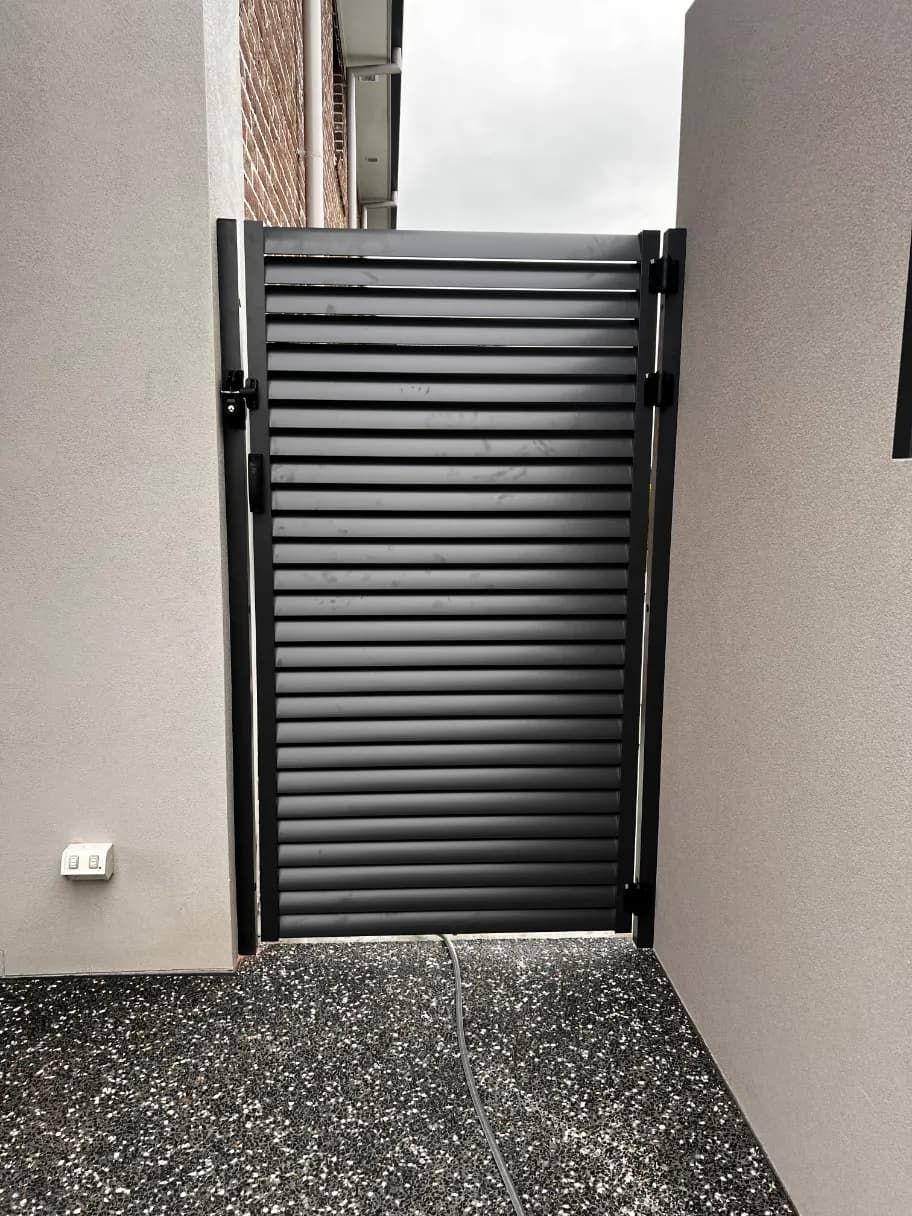 A Black Gate Is Sitting On The Side Of A Building Next To A WALL — Mid Coast Glass Fencing In Bonny Hills, NSW