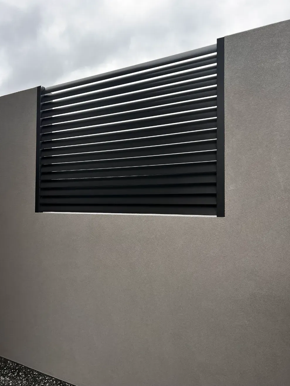 A Black Fence Is Sitting On Top Of A Gray WALL — Mid Coast Glass Fencing In Forster, NSW
