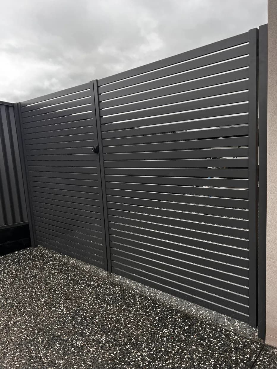 A Black Metal Fence With A Gate Is Surrounded By GraVEL — Mid Coast Glass Fencing In Hallidays Point, NSW