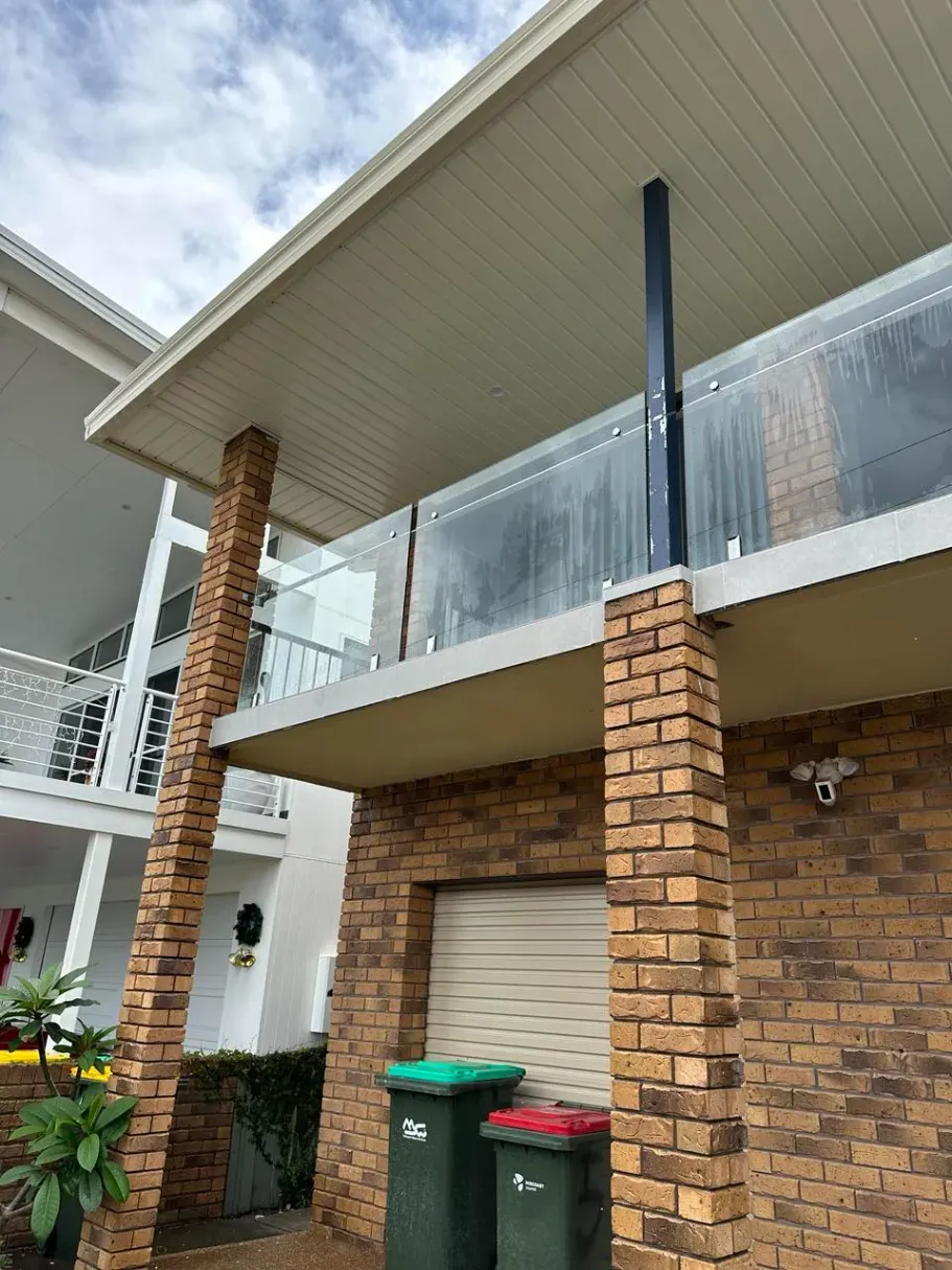 A Brick House With A Balcony And Trash Cans In Front Of IT — Mid Coast Glass Fencing In Hallidays Point, NSW