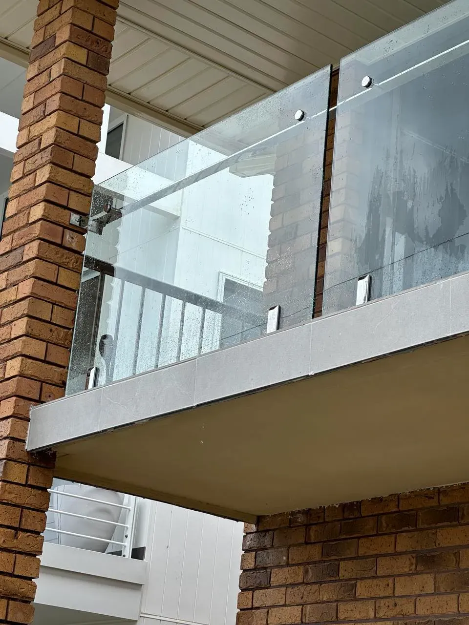 A balcony with a glass railing on a brick building — Mid Coast Glass Fencing In Taree, NSW