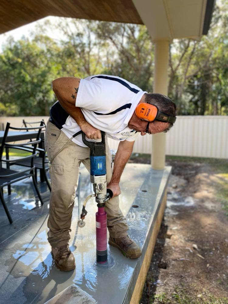 A man is using a drill to drill a hole in the ground — Mid Coast Glass Fencing In Old Bar, NSW