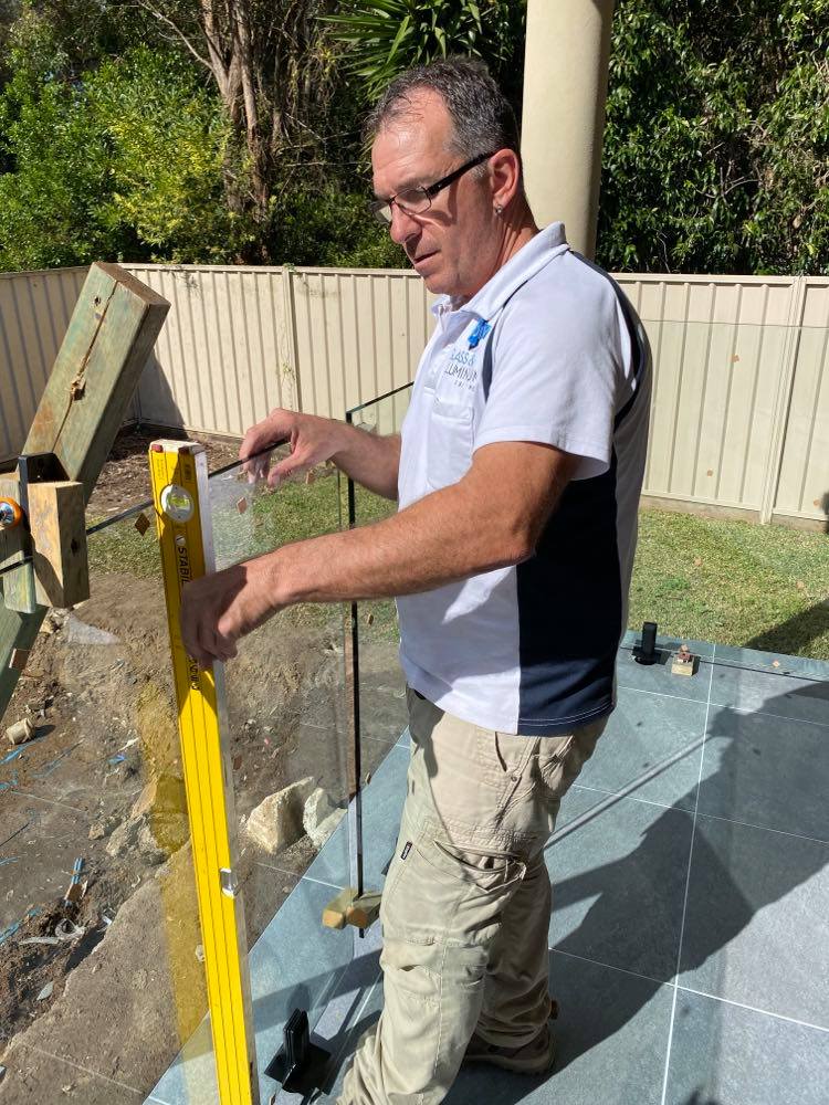 A man is using a yellow level to measure a glass railing — Mid Coast Glass Fencing In Old Bar, NSW