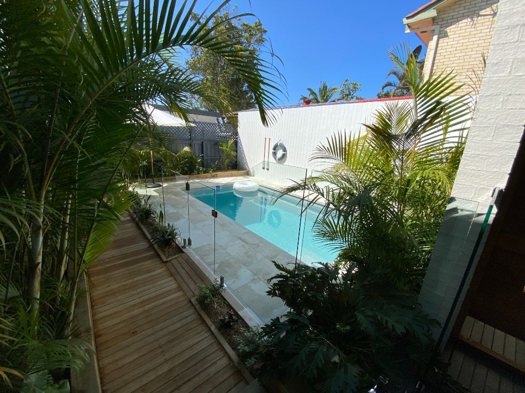 A large swimming pool is surrounded by trees and a wooden walkway — Mid Coast Glass Fencing In Old Bar, NSW