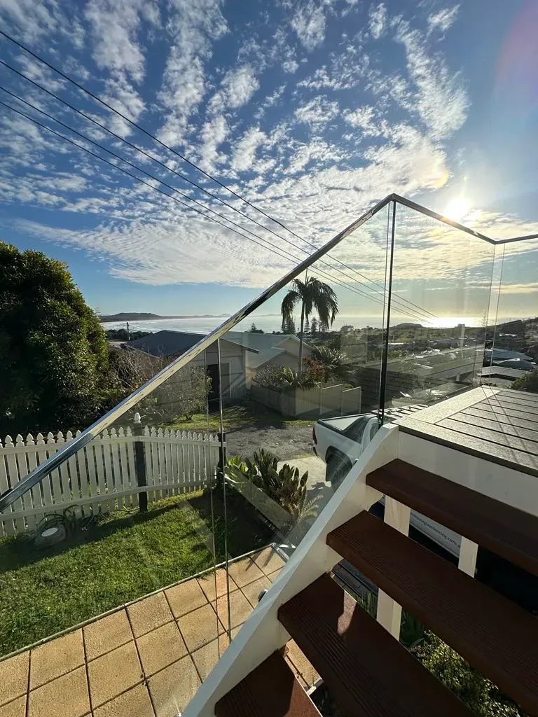 A set of stairs with a glass railing and a view of the ocean — Mid Coast Glass Fencing In Taree, NSW