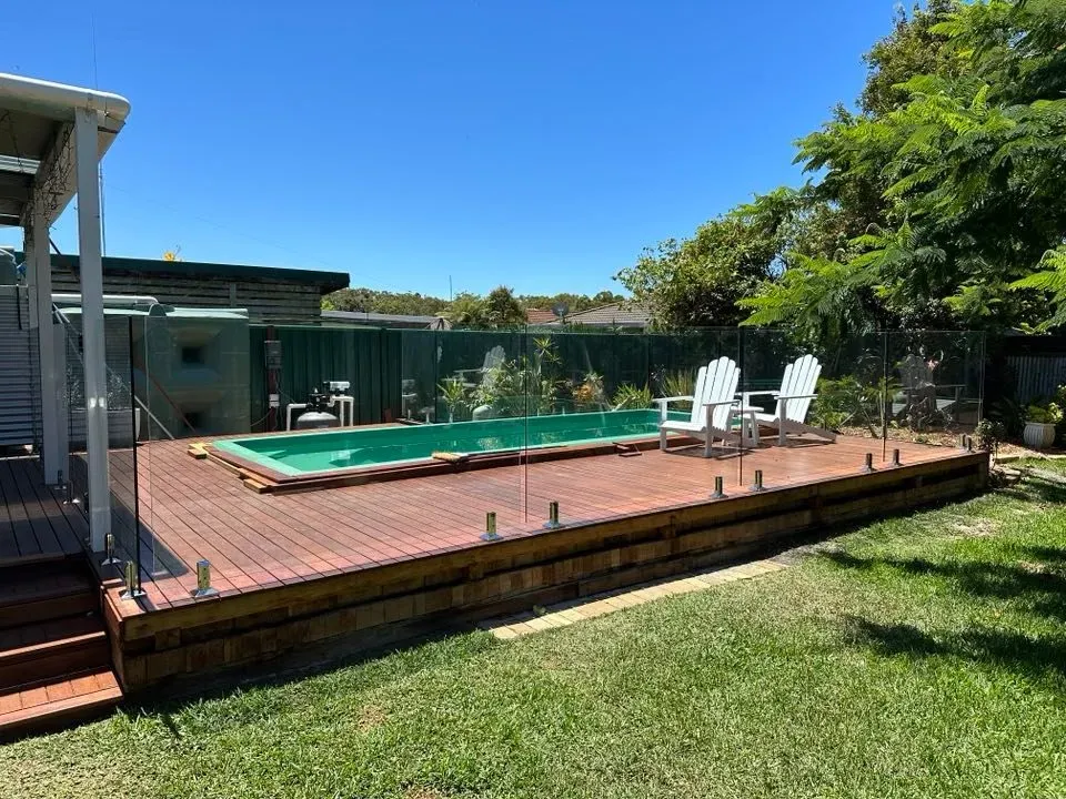A Large Swimming Pool Is Surrounded By A Wooden Deck And ChaIRS — Mid Coast Glass Fencing In Taree, NSW