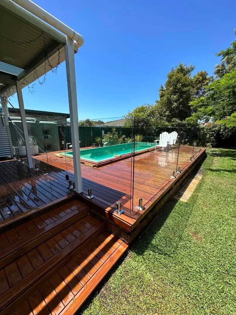 A Wooden Deck Next To A Swimming Pool In A BackyARD — Mid Coast Glass Fencing In Forster, NSW